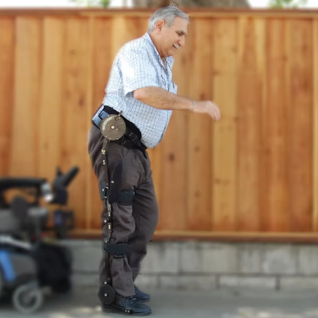 Man using a Kickstart a robotic exoskeleton in an outdoor setting with a wooden fence.